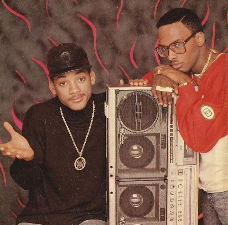 two men standing next to each other holding a boom box in front of a wall