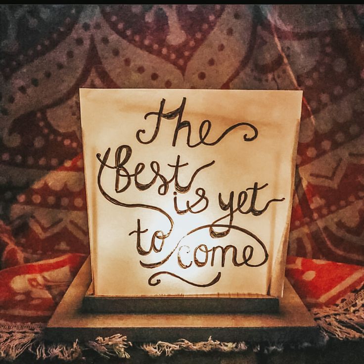 the best is yet to come light up sign on a wooden stand in front of a patterned wall