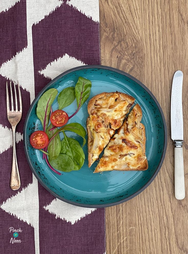 a blue plate topped with pizza next to a fork and knife on top of a wooden table