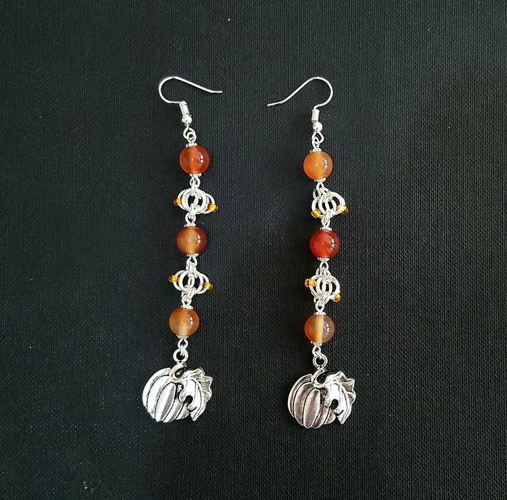 Silver plated chainmaille in a variation of butterfly weave, studded with orange glass seed beads, mirrors the shape of the focal points, two pumpkin charms. Round carnelian beads in varying shades of orange bring to mind the squash's vibrant colour. An ideal Halloween gift or autumnal accessory. Each earring is approximately 4.25 inches (10.6 cm) in length, with a drop length of 3.5 inches (8.7 cm). Nickel Free Carnelian Orange Earrings, Handmade Carnelian Orange Earrings, Handmade Orange Carnelian Earrings, Adjustable Nickel-free Carnelian Jewelry, Adjustable Nickel Free Carnelian Jewelry, Orange Jewelry With Silver Beads As A Gift, Orange Beaded Czech Glass Jewelry, Orange Jewelry With Silver Beads For Gift, Orange Sterling Silver Jewelry With Round Beads