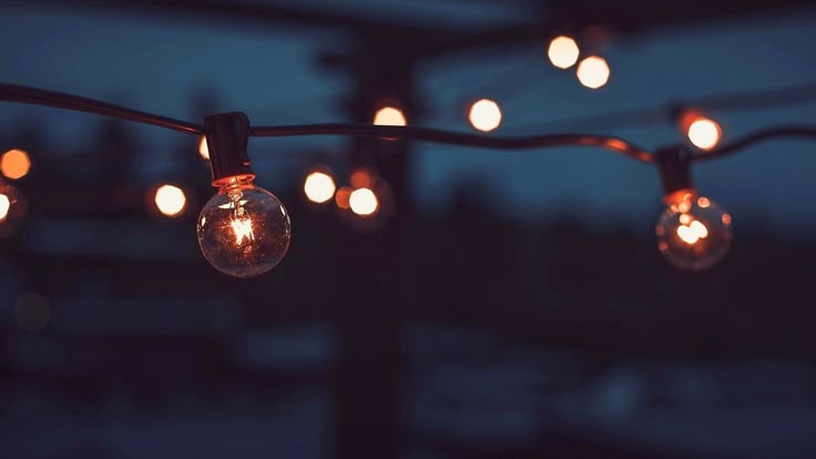 some light bulbs are hanging from a wire with lights on it in the night sky