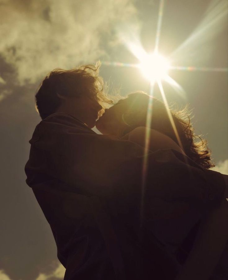 a man and woman kissing in front of the sun