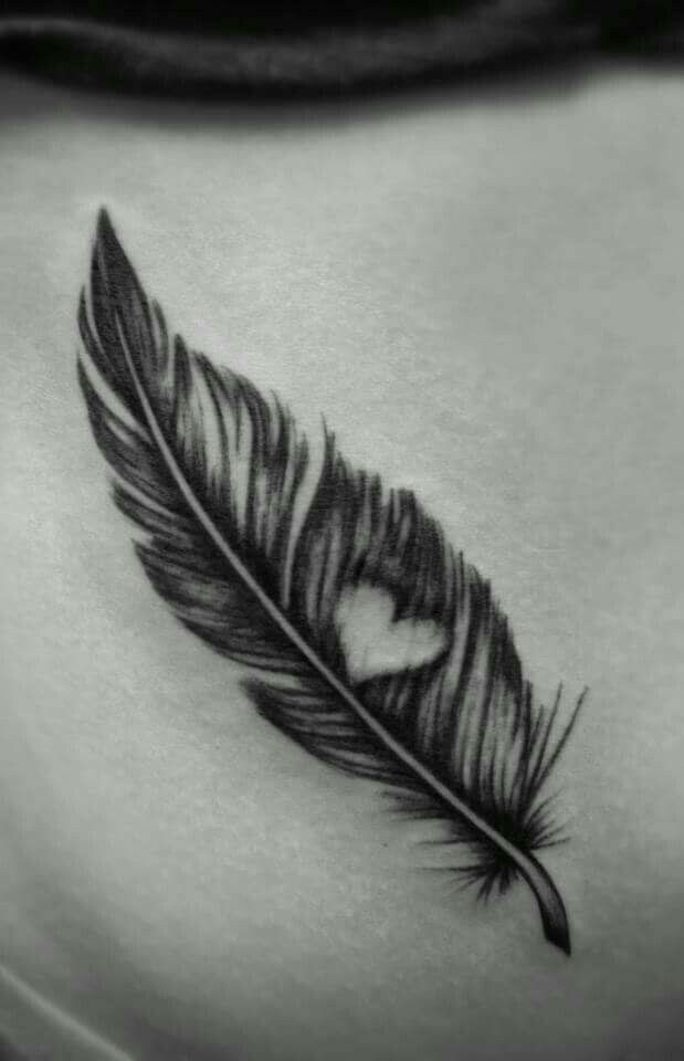 a black and white photo of a feather with a heart tattoo on the side of her stomach