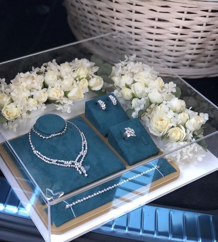 an assortment of jewelry on display in a glass case with flowers and basket behind it