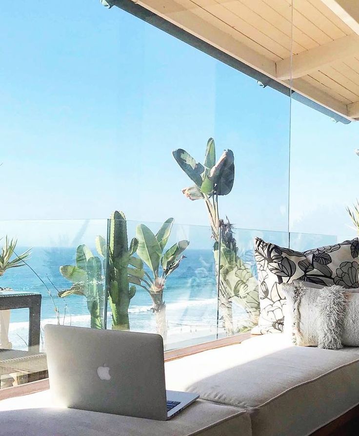 an open laptop computer sitting on top of a couch next to a glass wall covered in plants