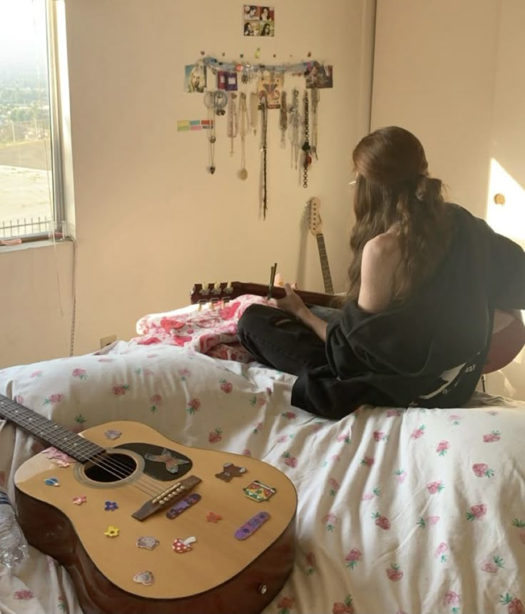 a person sitting on a bed with a guitar in front of them and a window