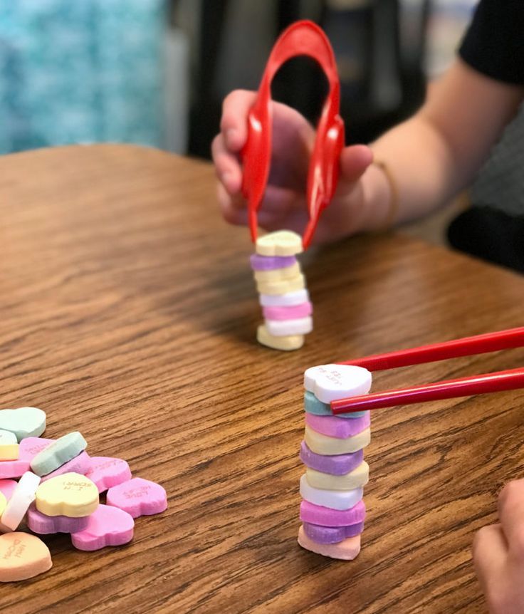 a child is playing with some candy and scissors on the wooden table next to them