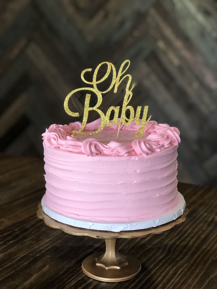 a pink and gold cake with the word oh baby on top sitting on a wooden table