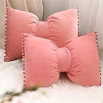 three pink pillows with scalloped edges on a white furnishing in front of a window