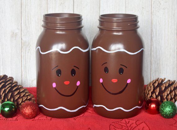 two brown jars with faces painted on them next to pine cones and christmas decorations,