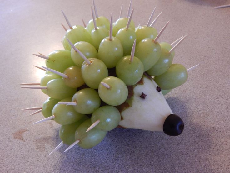 a hedgehog made out of grapes sitting on top of a counter next to an apple