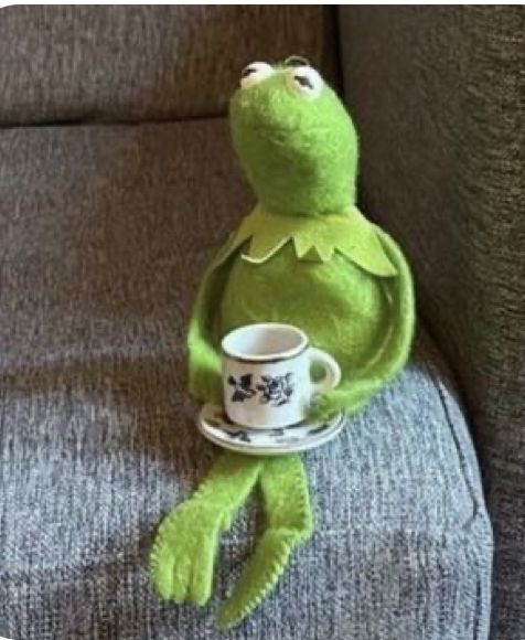 kermie the frog sitting on a couch holding a coffee cup