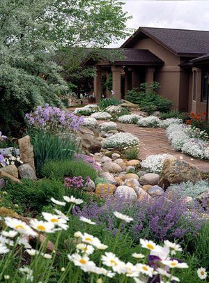 a garden with flowers and rocks in front of a house