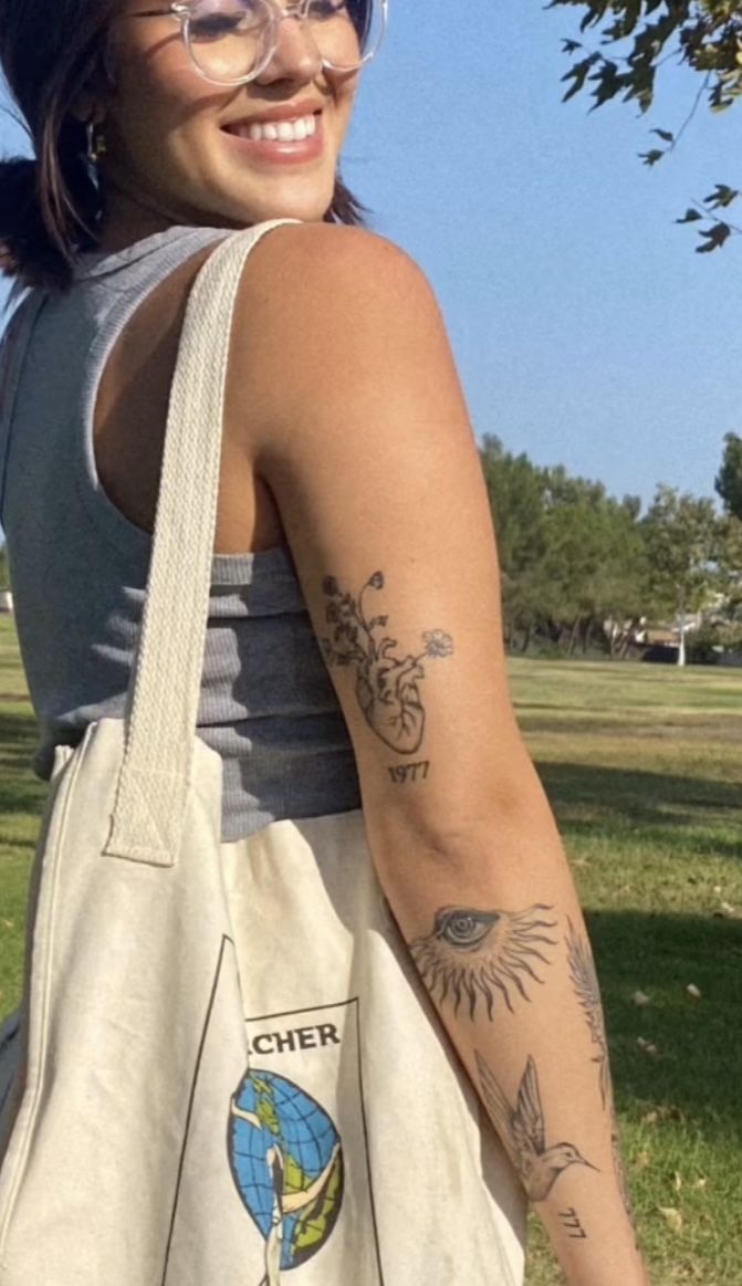 a woman holding a white bag with tattoos on her arm and shoulder, in the park