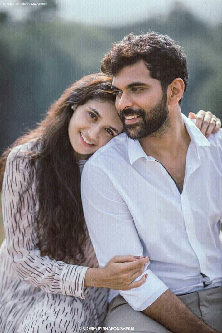 a man and woman sitting next to each other in front of the camera with their arms around each other