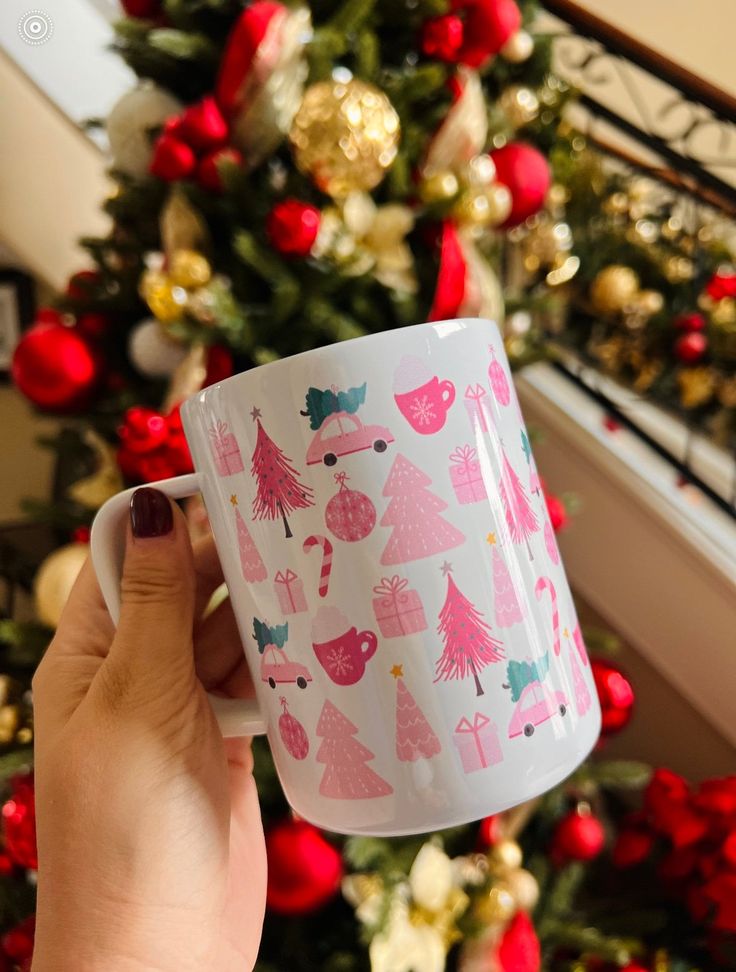 a person holding up a coffee mug in front of a christmas tree with red and gold ornaments