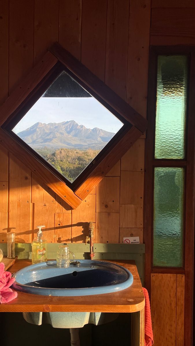 there is a sink in the corner of this bathroom with a mountain view through it