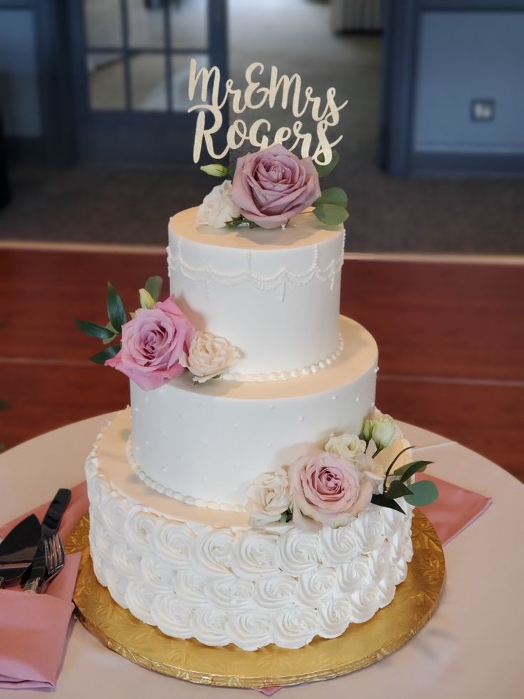 a wedding cake with pink flowers and mr and mrs signs on top is sitting on a table