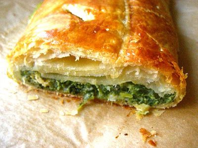 a close up of a pastry with spinach and cheese in it on a piece of wax paper