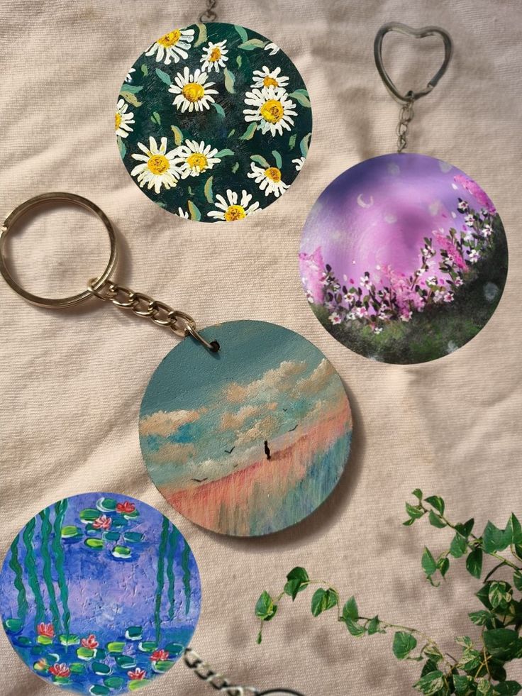 four key chains with paintings on them sitting next to a potted plant and flowers