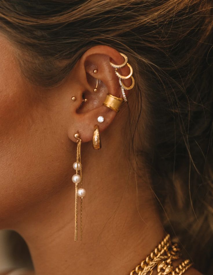 a close up of a person wearing gold ear cuffs and earrings with pearls on them