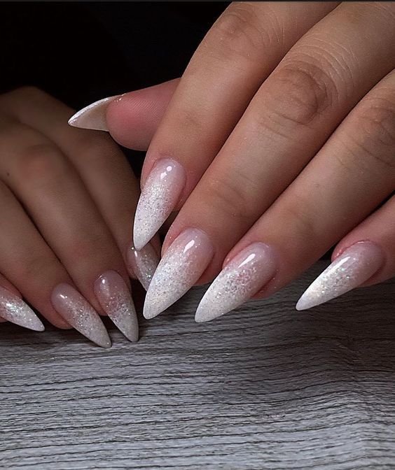 a woman's hands with long white nails and glitter on their fingertipss, holding onto a wooden table