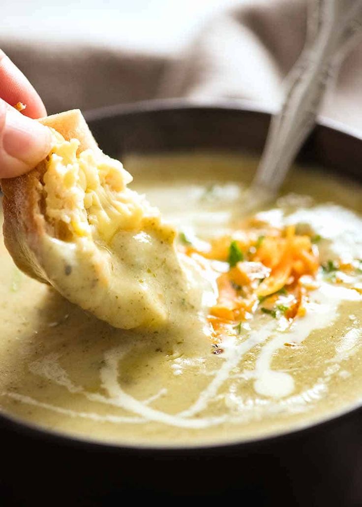 a person dipping some kind of food into a bowl with broccoli and cheese