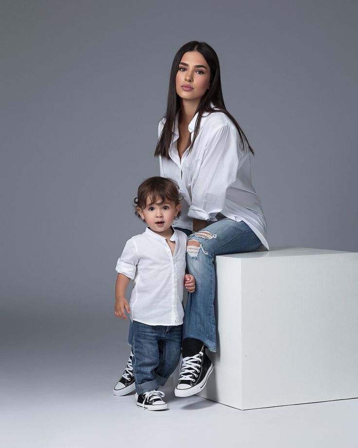 a woman sitting on top of a white box next to a little boy in jeans