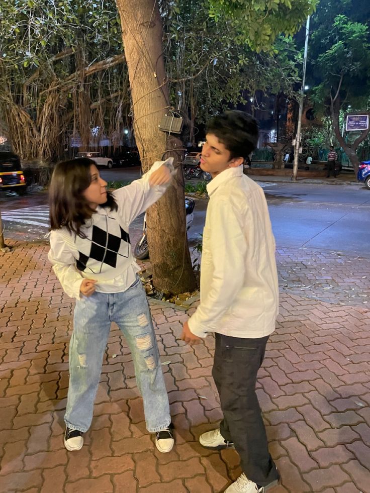 a man and woman standing next to each other on a brick walkway near a tree