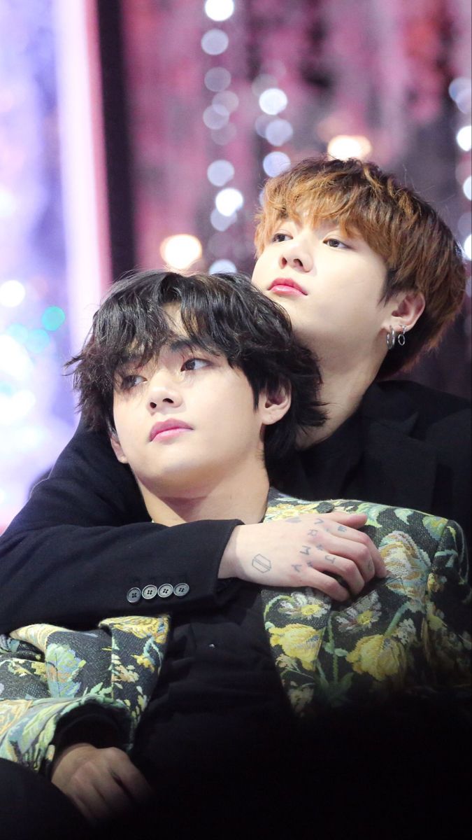 two young men sitting next to each other in front of a stage with lights behind them