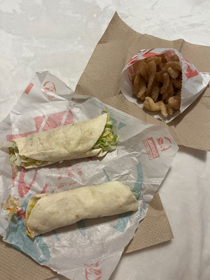 two burritos and some fries are sitting on paper wrappers next to each other