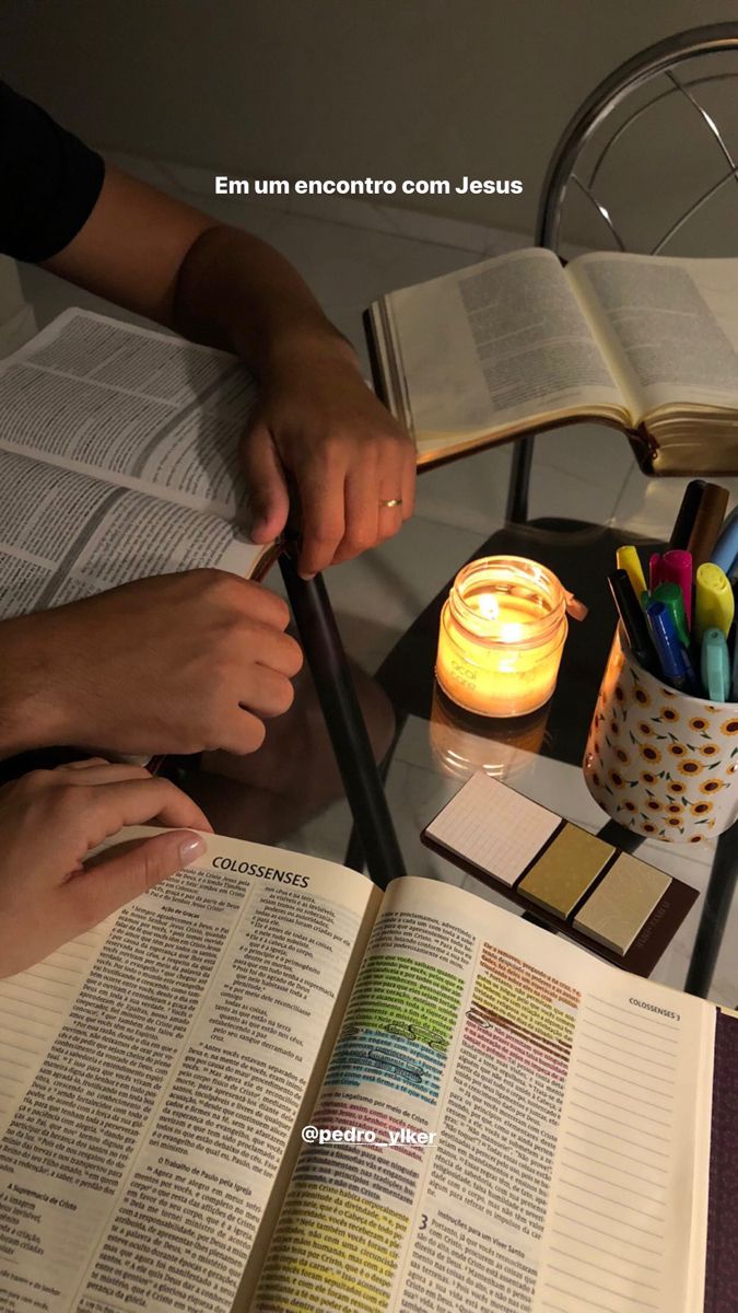 two people are sitting at a table with an open book and some colored pencils