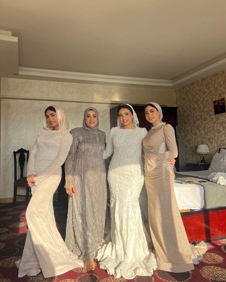 four women in long dresses standing next to each other on a carpeted room floor