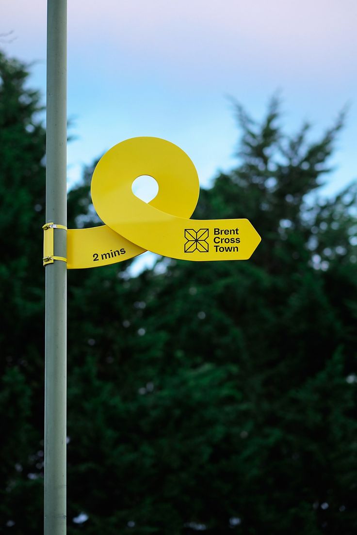 a pole with two yellow signs attached to it's sides and trees in the background