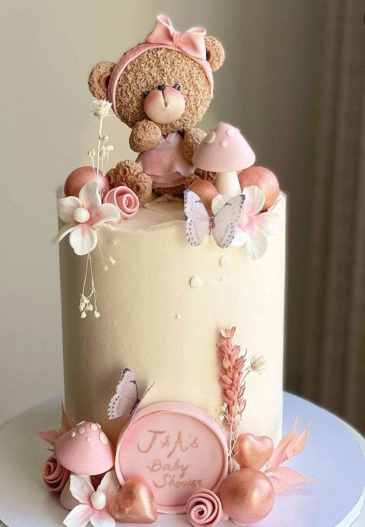 a teddy bear sitting on top of a cake with pink flowers and butterflies around it