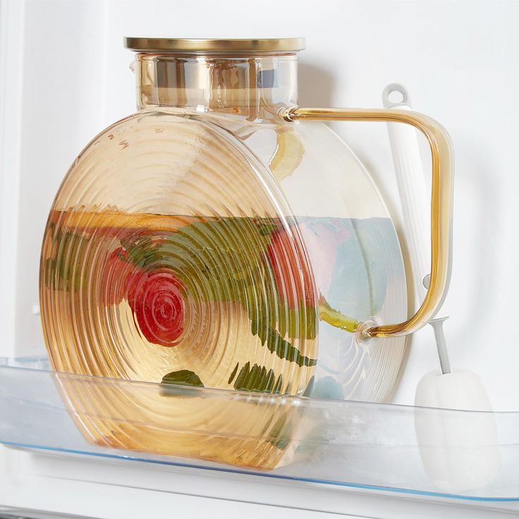 a glass container with a gold handle on top of a shelf next to a white wall