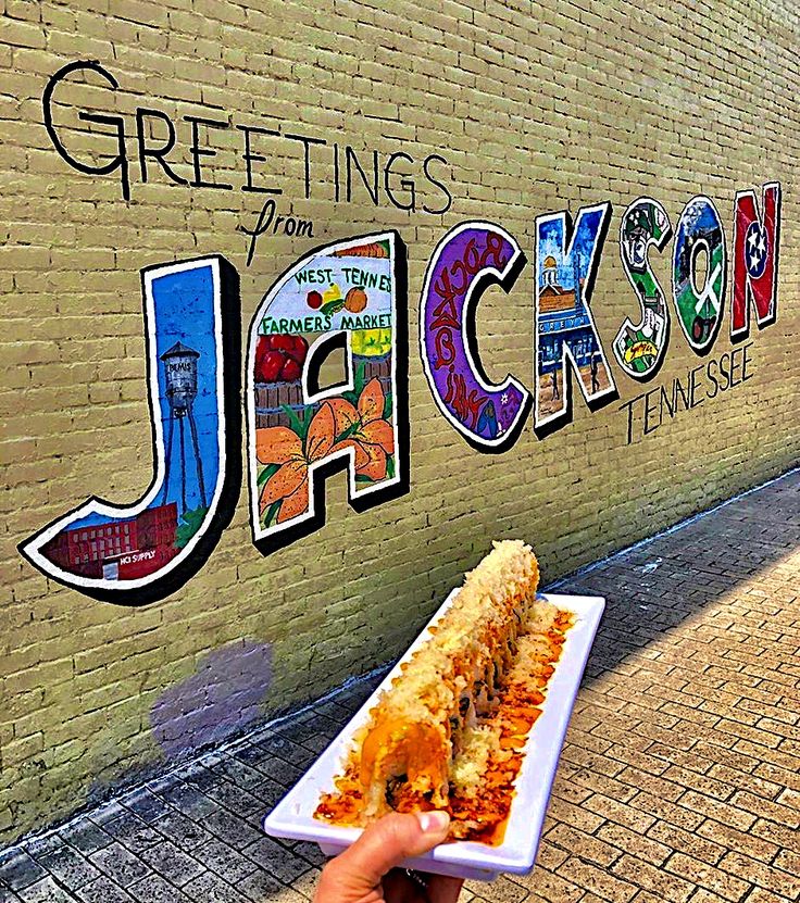 a person holding a plate with food in front of a brick wall that reads greetings from jackson