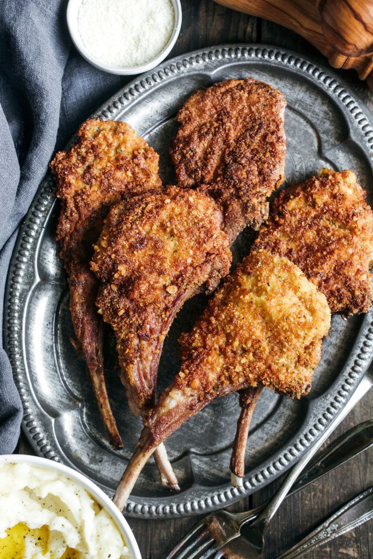 three pieces of fried chicken on a plate with mashed potatoes and butter in the background