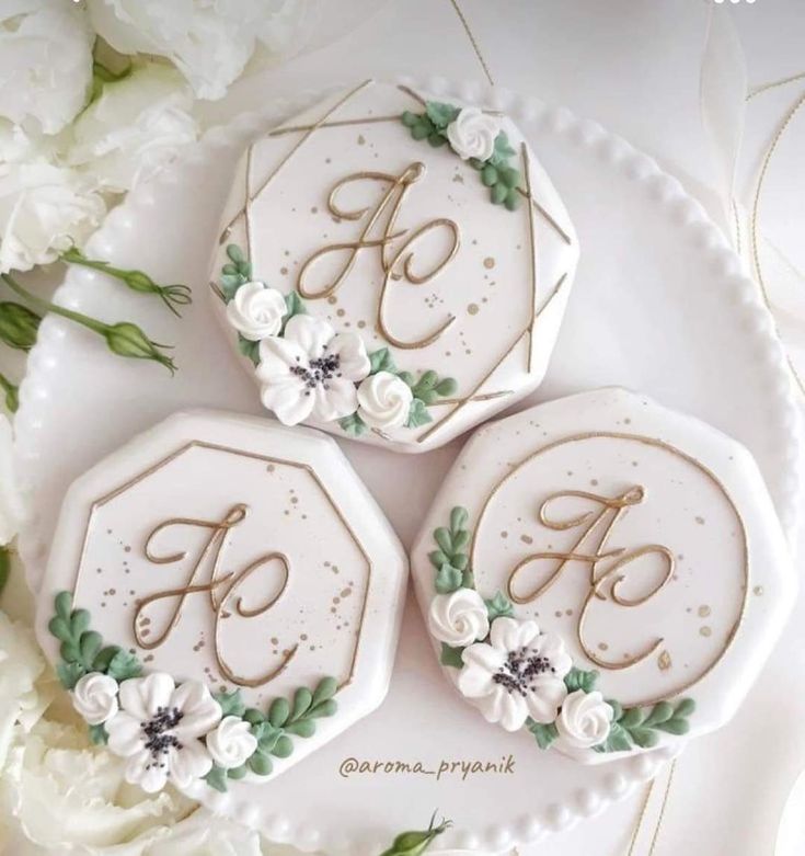 three cookies decorated with flowers and monograms on top of a white platter