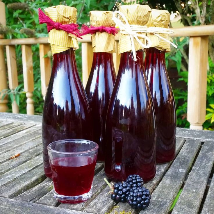 three bottles of liquid sitting on top of a wooden table next to a glass filled with blackberries