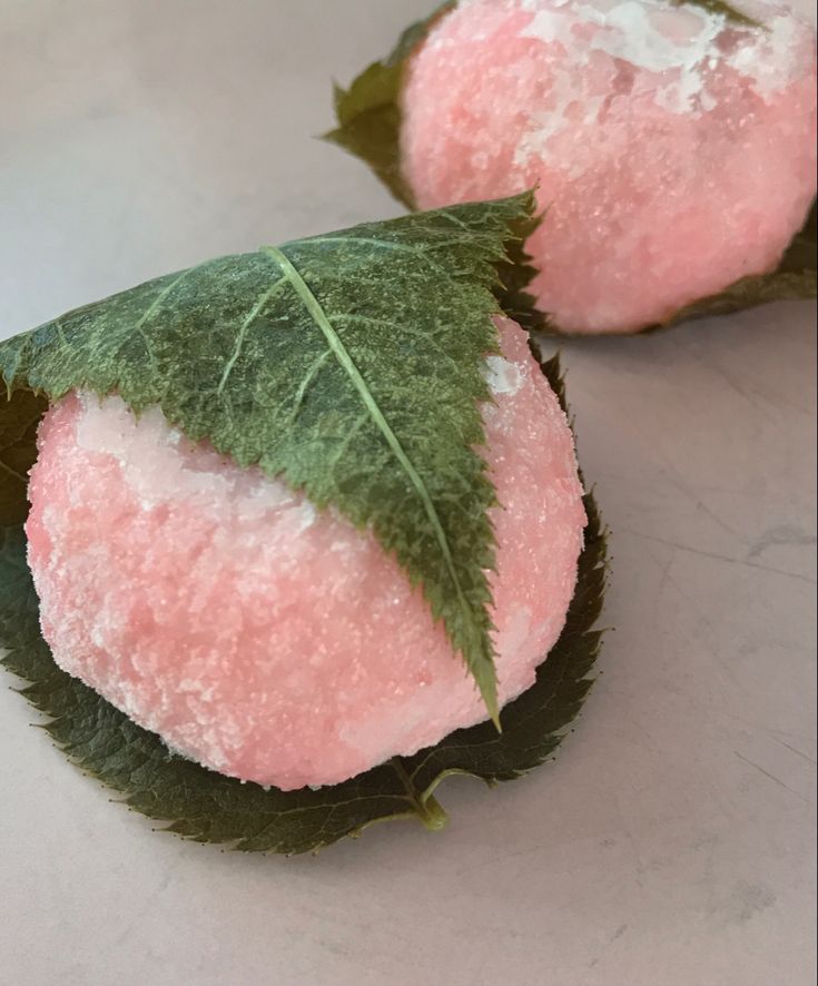 two pieces of fruit with green leaves on them sitting on top of a table next to each other