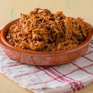 a bowl filled with shredded meat sitting on top of a table next to a fork