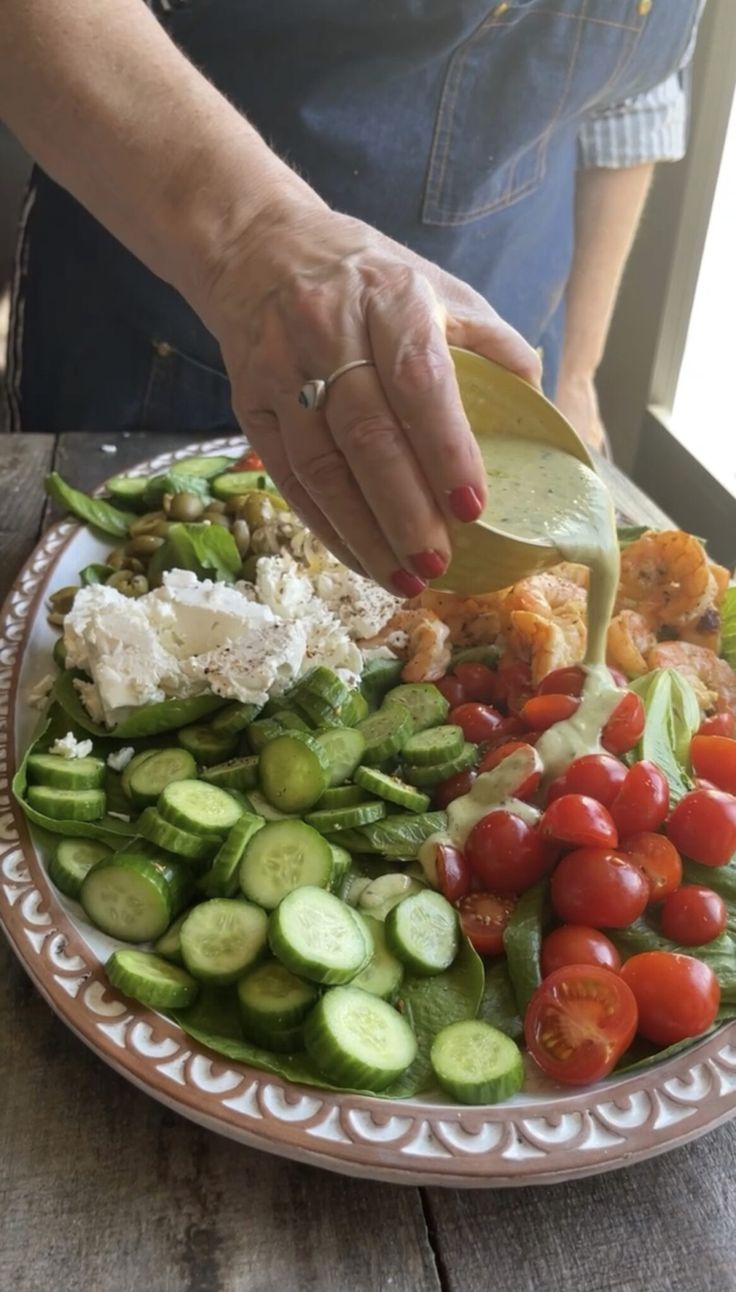 a person pouring dressing over a plate of vegetables