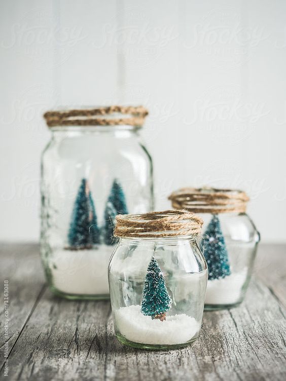 three glass jars filled with snow and small trees in them on top of a wooden table