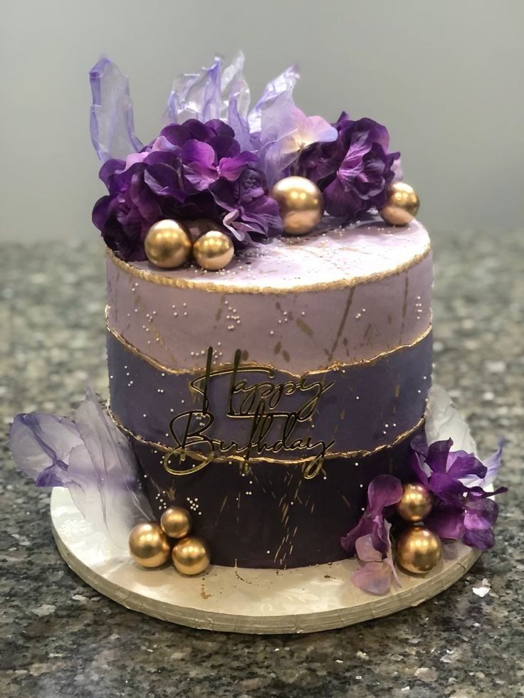 a purple and gold decorated cake on top of a marble counter with flowers in the middle