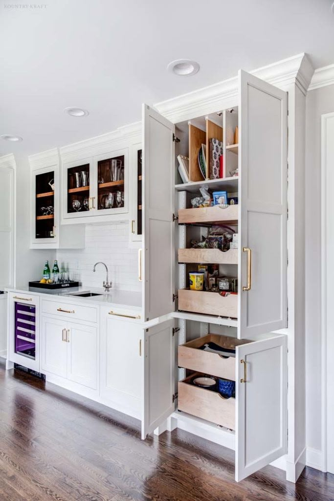 an open cabinet in the middle of a kitchen with wooden floors and white cabinets on both sides