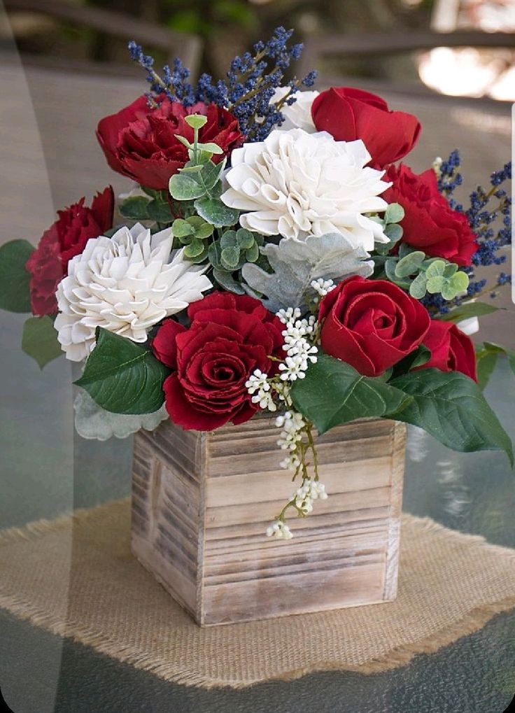 a bouquet of red, white and blue flowers in a wooden vase on a table