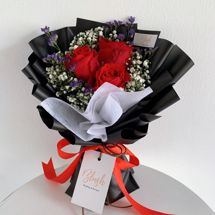 a bouquet of red roses and baby's breath wrapped in black paper with an orange ribbon