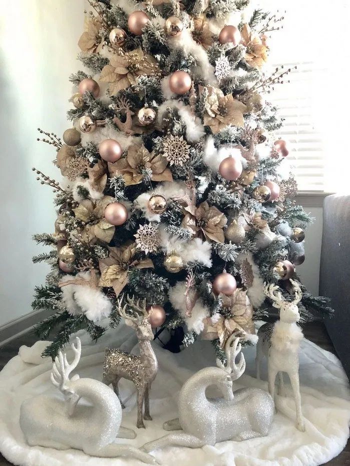 a white christmas tree with gold and silver ornaments on it's branches, surrounded by reindeer figurines