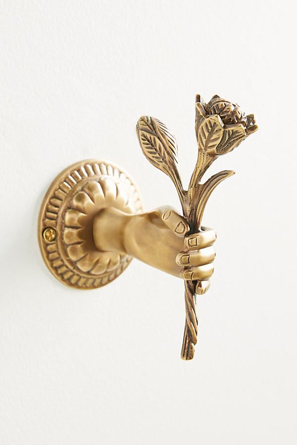 a gold colored flower shaped door handle on a white wall with a hand holding it